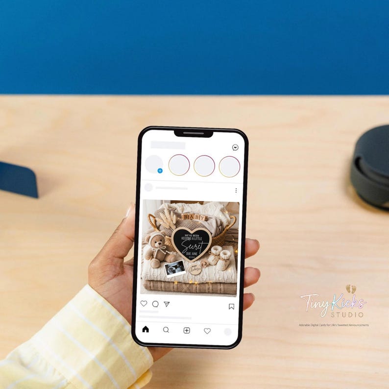 May include: A smartphone displays a digital pregnancy announcement. The announcement features a heart-shaped chalkboard with the words "We've been keeping a little secret" and "Due June". The image includes a teddy bear, baby shoes, and a sonogram.