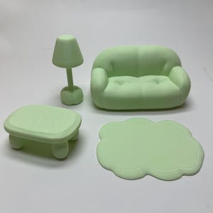 May include: A miniature, light green living room set. The set includes a sofa, a small table, a lamp, and a cloud-shaped rug. The furniture is made of a solid material and has a smooth finish. The lamp has a conical shade.