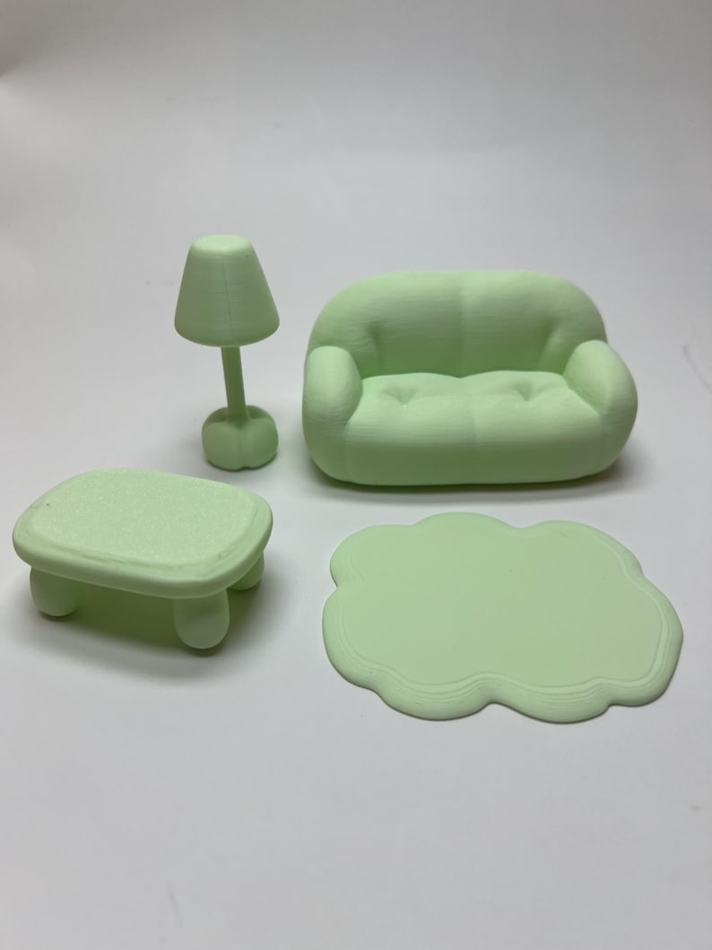 May include: A miniature, light green living room set. The set includes a sofa, a small table, a lamp, and a cloud-shaped rug. The furniture is made of a solid material and has a smooth finish. The lamp has a conical shade.