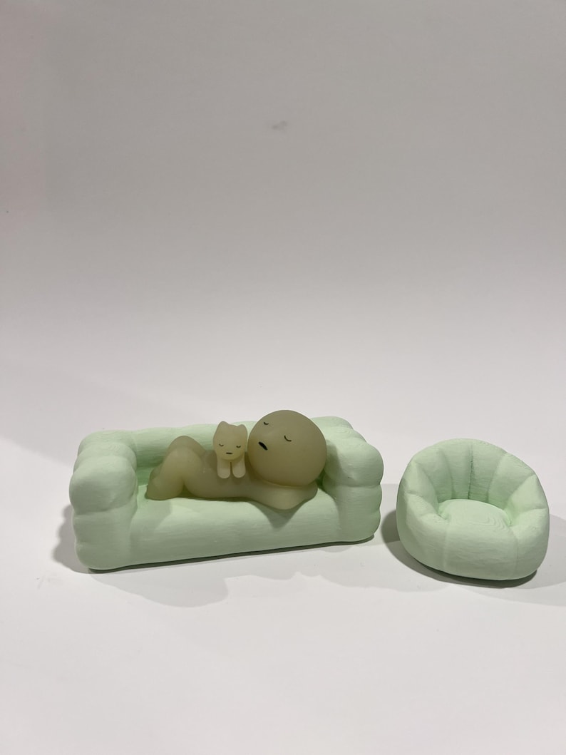 Puede incluir: Un sof&aacute; en miniatura verde claro con una figura y una figura de gato. La figura est&aacute; acostada en el sof&aacute;, con una figura de gato descansando sobre su pecho. Al lado del sof&aacute; hay un sill&oacute;n en miniatura verde claro a juego.
