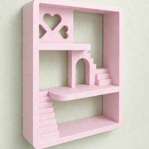 Könnte beinhalten: Ein rosa Wandregal mit einem einzigartigen architektonischen Design. Es verfügt über mehrere Ebenen, Treppen, einen gewölbten Durchgang und herzförmige Ausschnitte. Das Regal ist eine dekorative Aufbewahrungslösung, ideal für kleine Gegenstände.