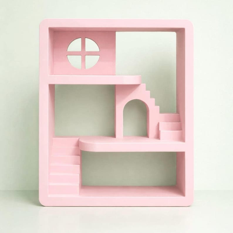 May include: A pink decorative shelf with a unique architectural design. It features a window, archway, stairs, and multiple levels. The shelf is a soft, pastel pink color and has a modern, minimalist aesthetic.