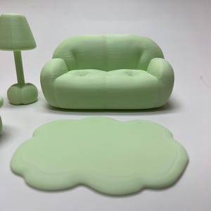 May include: A miniature mint green living room set, including a sofa, a lamp, and a cloud-shaped coffee table. The furniture is made of a solid material and has a smooth finish. The sofa has a rounded design with two armrests.