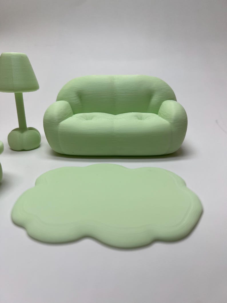 May include: A miniature mint green living room set, including a sofa, a lamp, and a cloud-shaped coffee table. The furniture is made of a solid material and has a smooth finish. The sofa has a rounded design with two armrests.