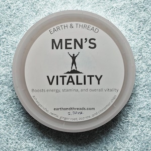 May include: A round, off-white container with a white label. The label reads "EARTH & THREAD MEN'S VITALITY" and features a silhouette of a person with arms raised. The text "Boosts energy, stamina, and overall vitality" is also present. The container is 65 grams.