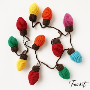 Puede incluir: Una guirnalda de luces navideñas hechas a mano con ganchillo. Las luces son de varios colores, incluyendo rojo, amarillo, naranja, verde, rosa y azul. Cada luz tiene una base marrón y está conectada por una cuerda marrón. Disposición circular.
