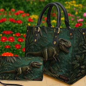 May include: A green handbag and matching wallet set with a detailed embossed Tyrannosaurus Rex design. The handbag has black handles and gold-coloured hardware. The wallet has a wrist strap. The background is a blurred floral garden.