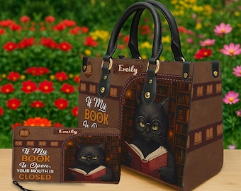 Puede incluir: Un conjunto de bolso y cartera marrones con un gato negro leyendo un libro en una biblioteca. El bolso y la cartera tienen el texto "If My Book Is Open. Your Mouth Is Closed." El conjunto tiene asas y detalles negros.