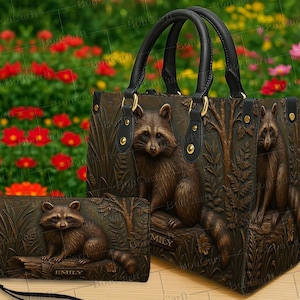 May include: A brown raccoon-themed handbag and wallet set. The handbag has black handles and gold-colored hardware. The raccoon and forest scene are embossed on the leather. The wallet has a wrist strap and the name "EMILY" is visible.