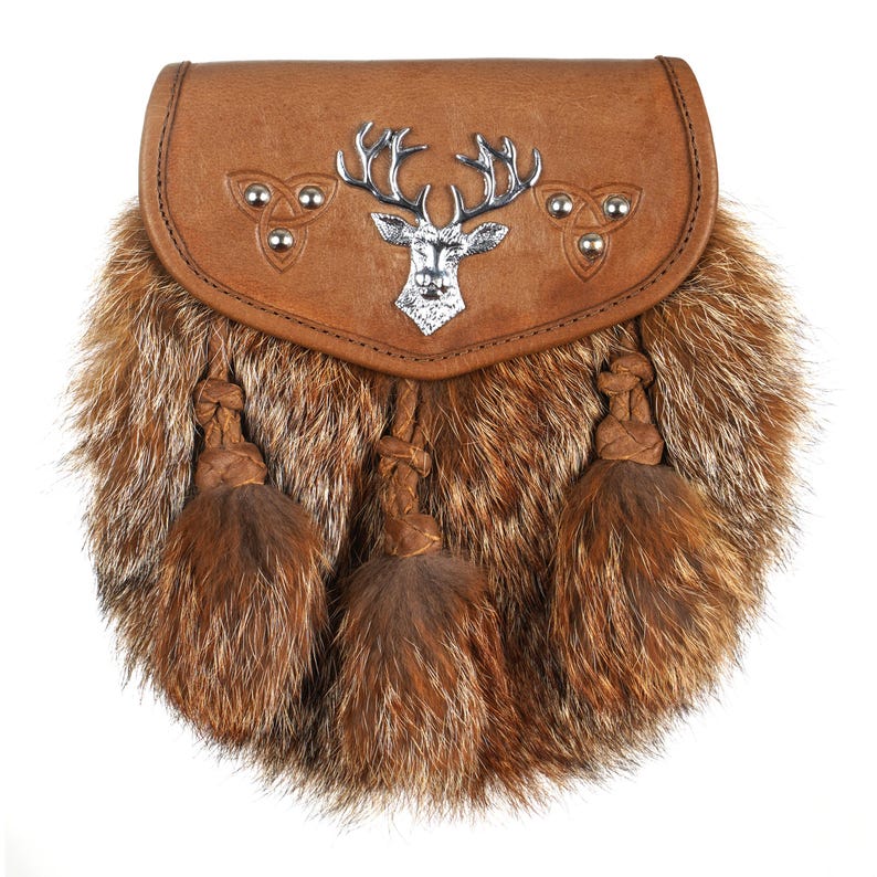 Puede incluir: Una sporran de cuero marr&oacute;n con un emblema de ciervo plateado y ribete de piel. La sporran tiene tres borlas marrones y detalles de nudos celtas. Este accesorio escoc&eacute;s tradicional se usa con un kilt.