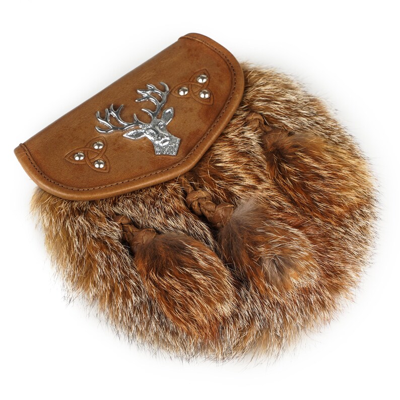 Puede incluir: Una sporran de cuero marr&oacute;n con un emblema de ciervo plateado y detalles de nudos celtas. La sporran presenta un cuerpo de piel y dos borlas decorativas. Este accesorio escoc&eacute;s tradicional se usa con un kilt.