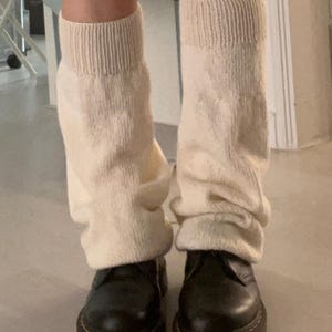 Puede incluir: Calentadores de punto color crema sobre botas de plataforma negras. Los calentadores son gruesos y acanalados en la parte superior, con un ajuste ligeramente holgado. Las botas tienen una suela gruesa con costuras amarillas.