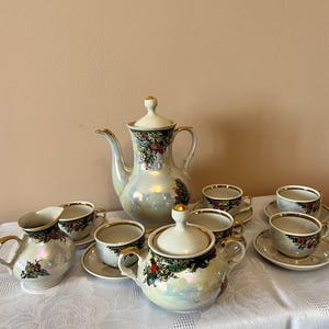 Puede incluir: Juego de té vintage con acabado nacarado. El juego incluye una tetera, azucarero, lechera y varias tazas y platillos. Cada pieza está decorada con un diseño floral y de bayas y ribete dorado.