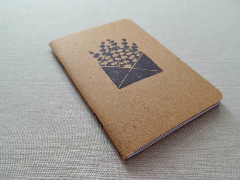 May include: A small brown notebook with a white spine. The cover has a black ink stamp of a bouquet of flowers in an envelope.