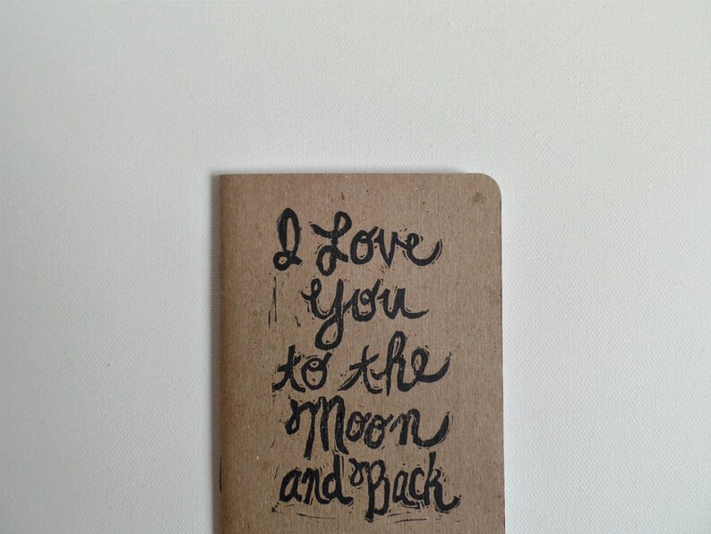 May include: A brown paper notebook with the handwritten message "I love you to the moon and back" in black ink.