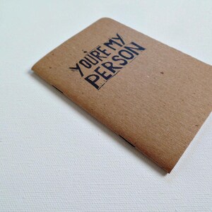 Op de afbeelding: Een bruin notitieboekje met de tekst "YOU'RE MY PERSON" in zwart gedrukt.