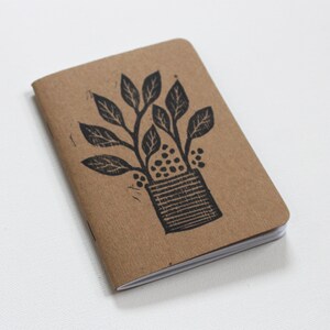 May include: A small brown notebook with a black and white illustration of a plant in a pot on the cover.