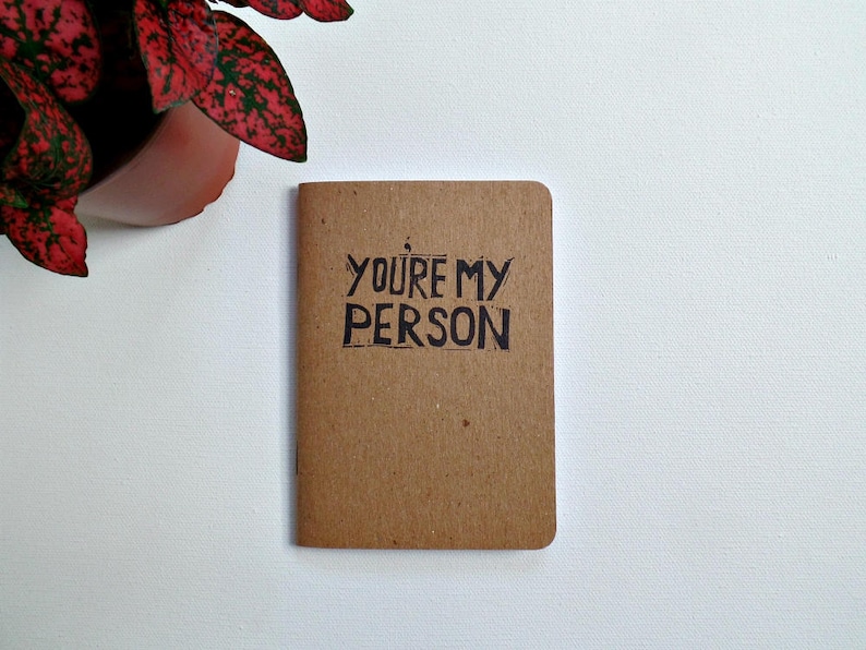 Op de afbeelding: Een klein bruin notitieboekje met de woorden "You're my person" geschreven in zwarte inkt.