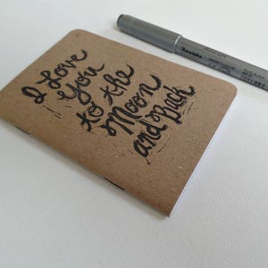 May include: A brown notebook with the handwritten message "I love you to the moon and back" on the cover.
