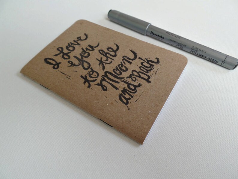 May include: A brown notebook with the handwritten message "I love you to the moon and back" on the cover.
