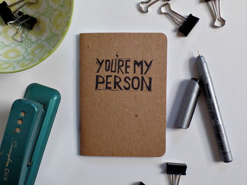 Op de afbeelding: Een klein bruin notitieboekje met de woorden "YOU'RE MY PERSON" in zwarte inkt op de voorkant.