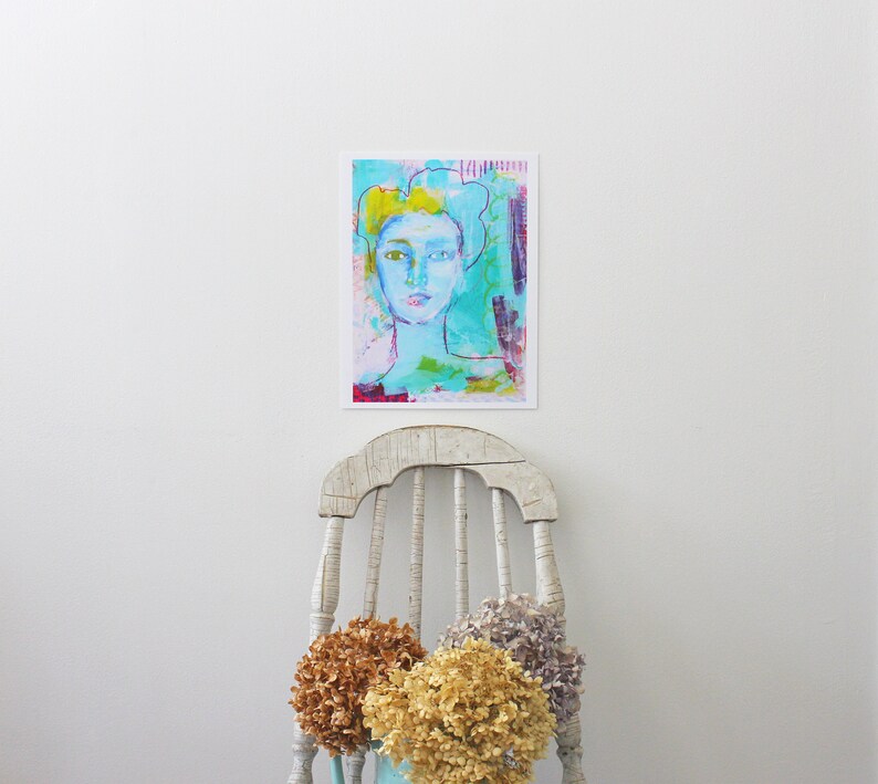 May include: Abstract art print featuring a woman's face with blue, green, and yellow hues. The artwork is mounted on a white background. A distressed white chair and dried flowers in shades of brown, yellow, and purple are in the foreground.