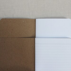 May include: A brown paper notebook with a white lined interior. The notebook is open to reveal the lined pages.