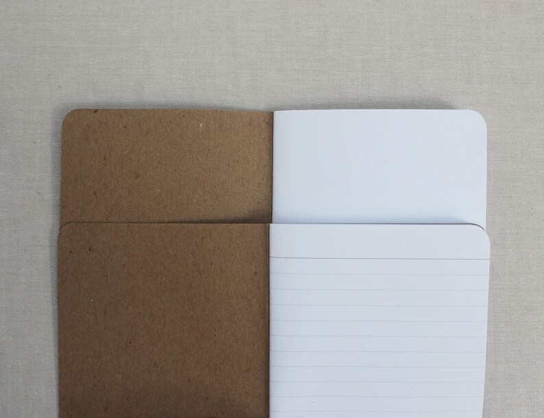 May include: A brown paper notebook with a white lined interior. The notebook is open to reveal the lined pages.