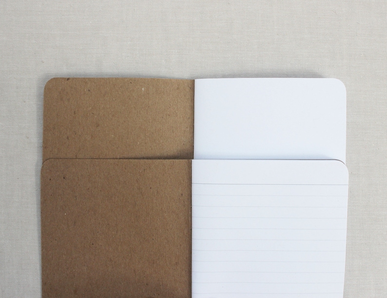 K&ouml;nnte beinhalten: Ein braunes Papiernotizbuch mit einem wei&szlig;en, linierten Innenleben. Das Notizbuch ist ge&ouml;ffnet, um die linierten Seiten zu zeigen.