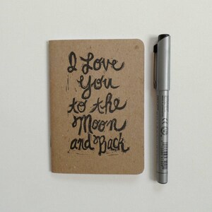 May include: A small brown notebook with the handwritten message "I love you to the moon and back" on the front.