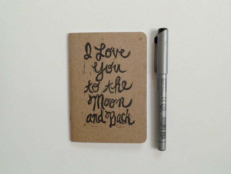 May include: A small brown notebook with the handwritten message "I love you to the moon and back" on the front.