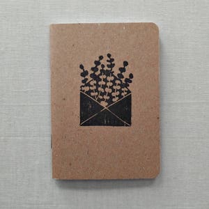 May include: A brown notebook with a black illustration of a plant growing out of an envelope.