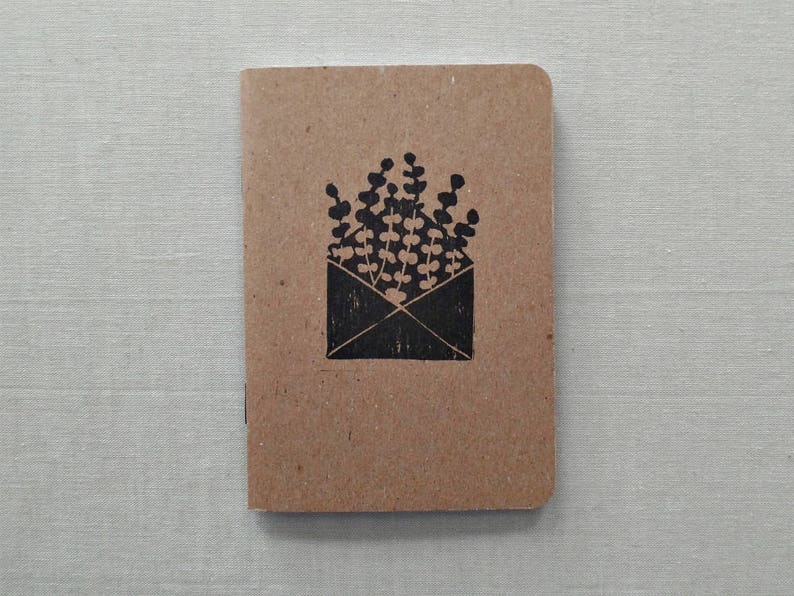 May include: A brown notebook with a black illustration of a plant growing out of an envelope.