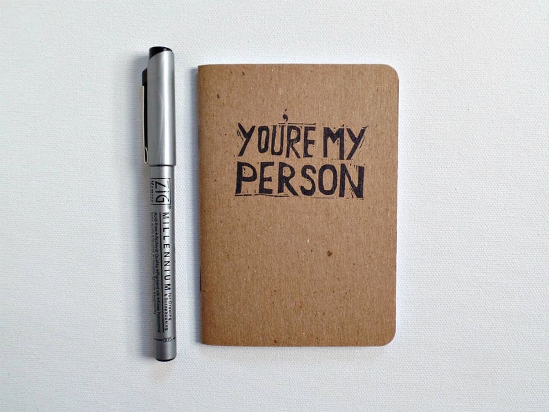 Op de afbeelding: Een klein bruin notitieboekje met de woorden "You're my person" in zwarte inkt op de voorkant.