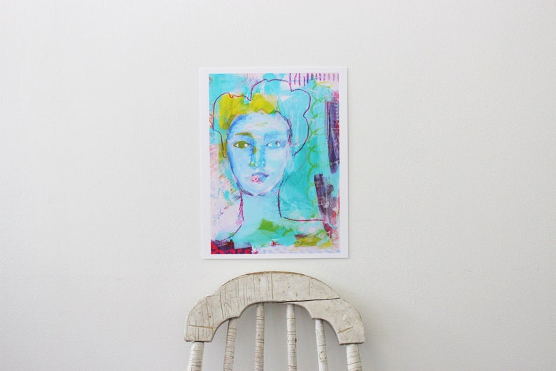 May include: Abstract art print featuring a portrait of a person with a light blue face and yellow hair. The artwork uses a mix of colors, including turquoise, pink, and purple. The art print is displayed on a white wall.