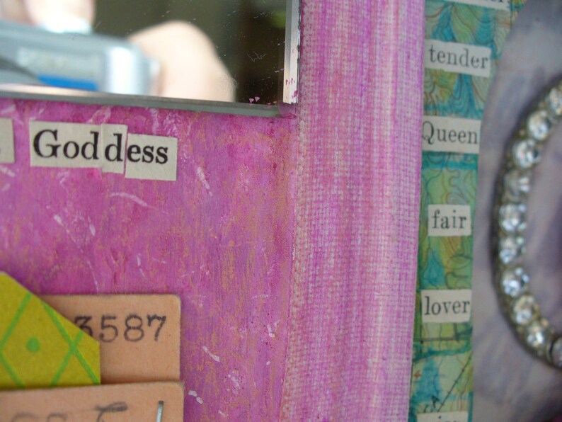May include: Close-up of a mixed media artwork with a vibrant pink background. The word "Goddess" is spelled out in cut-out letters. Other text includes "tender," "Queen," and "fair." A decorative element with rhinestones is visible.