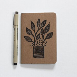 May include: A brown notebook featuring a black ink illustration of a potted plant with leaves and a textured pot.