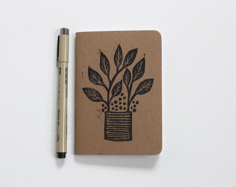 May include: A brown notebook featuring a black ink illustration of a potted plant with leaves and a textured pot.