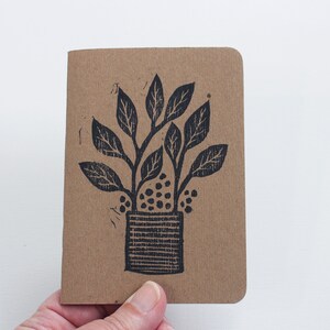 May include: A small brown notebook with a black ink illustration of a potted plant with leaves and berries.