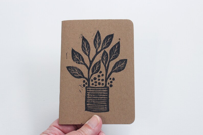 May include: A small brown notebook with a black ink illustration of a potted plant with leaves and berries.