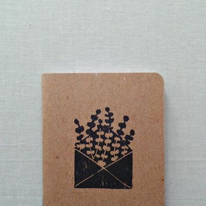 May include: A brown paper notebook with a black ink illustration of a bouquet of flowers in an envelope.