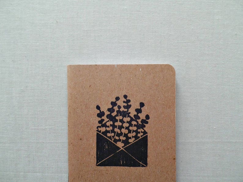 May include: A brown paper notebook with a black ink illustration of a bouquet of flowers in an envelope.