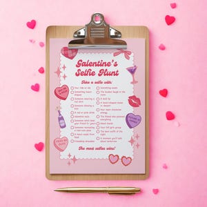 May include: A pink clipboard with a "Galentine's Selfie Hunt" checklist, featuring hearts, stars, and illustrations. The checklist includes prompts like "Someone wearing a red shirt" and "Heart hands." A gold pen rests below.