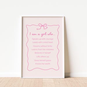Peut inclure: Impression encadrée avec un fond rose et une bordure décorative rose. Le texte "I am a girl who..." est en haut, suivi de phrases inspirantes. L'impression est dans un cadre blanc.