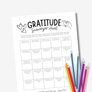 May include: A white paper sheet titled Gratitude Scavenger Hunt with a grid of prompts for writing or drawing. The header features heart illustrations and a hand-drawn heart shape. A cluster of colored pencils in yellow, red, blue, purple, and pink rests nearby.