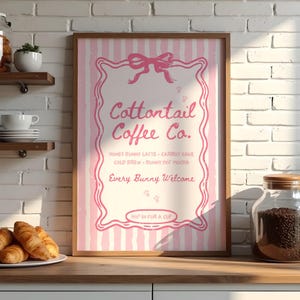 May include: A framed pink and white striped sign for Cottontail Coffee Co. The sign features a pink bow, decorative border, and the text: Honey Bunny Latte, Carrot Cake, Cold Brew, Bunny Hot Mocha, and Every Bunny Welcome. The sign is in a kitchen setting.
