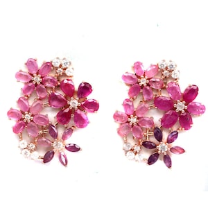 Peut inclure: Une paire de boucles d'oreilles en forme de fleurs. Chaque boucle d'oreille présente un groupe de pierres précieuses roses et violettes, avec des pierres d'accent claires. Les boucles d'oreilles ont un sertissage en or rose.