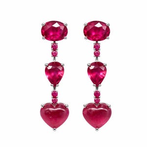 May include: A pair of elegant drop earrings featuring vibrant red gemstones. Each earring has an oval-shaped top stone, a pear-shaped middle stone, and a heart-shaped bottom stone, all connected by smaller round stones, set in a silver metal.