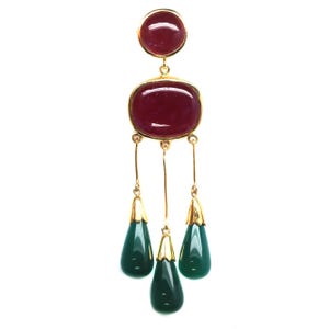 Pode incluir: Pingente dourado com uma pedra retangular granada e uma pedra redonda menor. Três pedras verdes em forma de gota com tampas douradas pendem abaixo. O pingente está em um fundo branco.