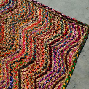 Può includere: Un tappeto intrecciato multicolore con un motivo a zig-zag. Il tappeto presenta una miscela di colori vivaci tra cui arancione, rosa, blu e verde. Il tappeto è realizzato con fibre naturali e ha un aspetto strutturato, adatto per l'arredamento della casa.